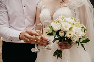 The bride in a white beaded dress and the groom in a white shirt are holding glasses of champagne...
