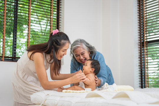 Happy multigenerational Asian family bonding time with baby at home, Grandmother, mother, and baby smiling together in bedroom, Three generations spending quality time at home