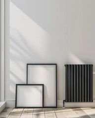 Obraz premium Two empty black frames leaning against a white wall with sunlight streaming through a window