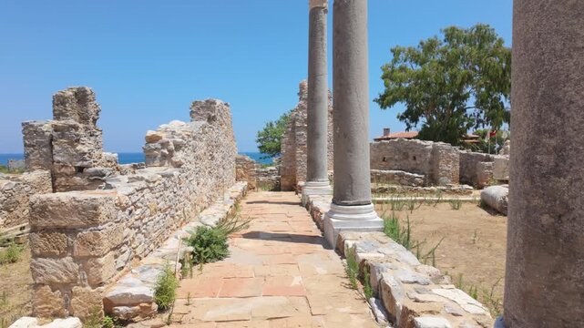 Camera moving forward between columns at the Anemurium Ancient City in Anamur, Mersin, Turkey. Historical ruins along the colonnaded street with a sea view on a sunny day.