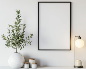 A blank black frame with an olive branch. a table lamp. and three jars on a white surface