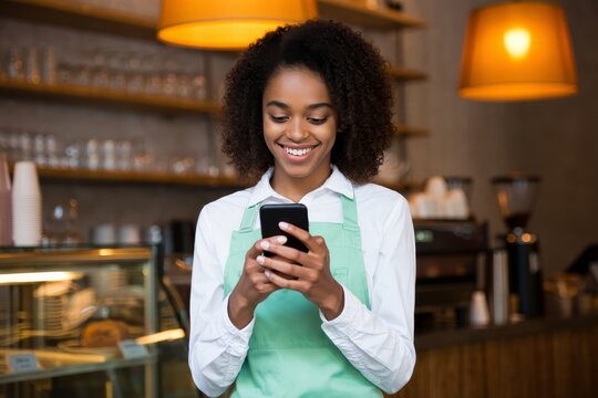 Young african american barista using mobile phone for orders in a coffee shop cafe