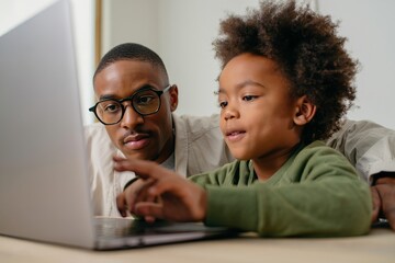 Father and son using laptop together at home for online learning and entertainment