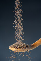 Brown cumin seeds fall from above onto a wooden spoon, ideal for aromatic seasoning and exotic...