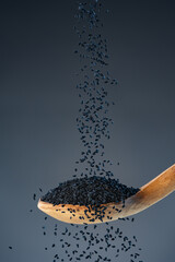 Black nigella seeds fall from above onto a wooden spoon, ideal for spice, seasoning and exotic...