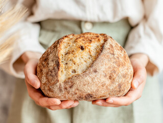 Hands hold a rustic loaf of bread in a cozy kitchen setting with a warm background
