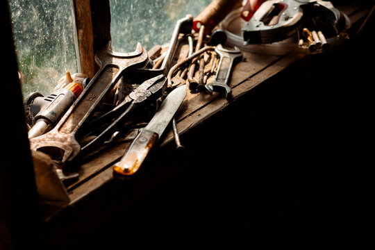 On the wooden surface by the window lie old tools: hammers, screwdrivers, wrenches, a knife and a drill. Light falls through the glass, creating a warm atmosphere.