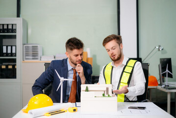 Engineer and businessman collaborate on sustainable energy with solar panels, wind turbines, and...