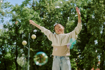 Portrait of Asian child girl smiling with arms raised standing outdoors in park surrounded by green trees and sunlight, enjoying playful moment during school outing