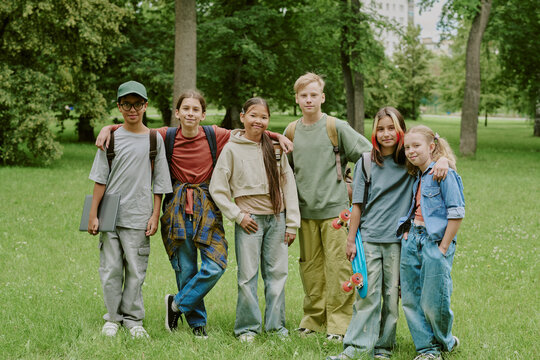 Fototapeta Group of diverse teenagers standing together in park, smiling and posing for camera, multiethnic boys and girls with backpacks and skateboard enjoying outdoor school activity