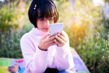 Cute little girl is using the smart phone. grass on background. On girl a hairpin with a pumpkin