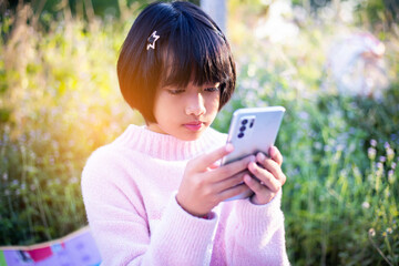 Cute little girl is using the smart phone. grass on background. On girl a hairpin with a pumpkin