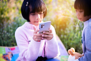 Cute little girl is using the smart phone. grass on background. On girl a hairpin with a pumpkin