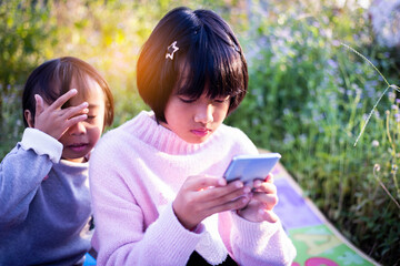 Cute little girl is using the smart phone. grass on background. On girl a hairpin with a pumpkin