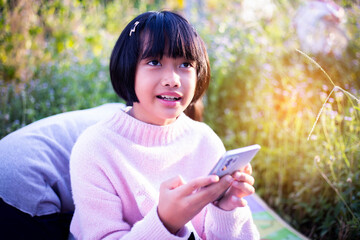 Cute little girl is using the smart phone. grass on background. On girl a hairpin with a pumpkin