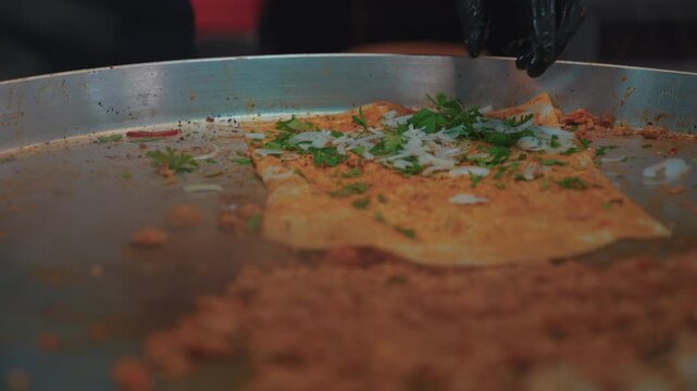 Close-up of a chef preparing a traditional Turkish tantuni wrap. The cook adds parsley, onions, tomatoes, and spicy minced meat to the flatbread (lavaş) on a hot griddle and rolls it.