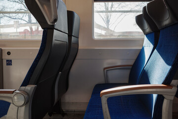 The interior of a train with empty blue fabric seats bathed in bright sunlight from the window. 
