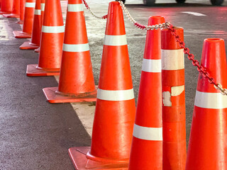 Close-up of multiple orange traffic cones connected with white and red chain, placed on the...