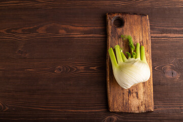 Fresh Fennel bulb on wooden cutting board on brown wooden, top view, copy space