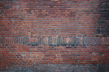 A full frame, close-up photograph of an aged brick wall featuring a mix of red and darker bricks, showcasing different patterns and textures.
