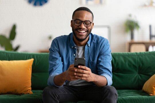 Happy african american man using smartphone at home on sofa for social media and chat