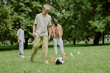 Group of multiethnic boys playing soccer in park with middle aged Black man supervising activity,...