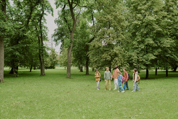 Group of multiethnic children and young Caucasian woman teacher walking together in green park,...