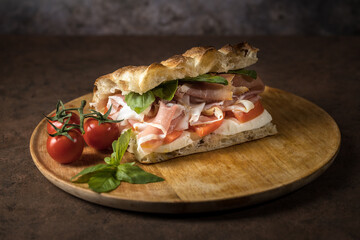 Delicious sandwich with sliced meet and tomato cherry on the wooden board.