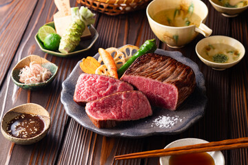 【黒毛和牛ステーキ】レアで美しく焼き上げた黒毛和牛モモ肉のステーキ。ジューシーな肉の旨みを引き立てるのは、素揚げした季節の野菜と彩り豊かな薬味。わさびや塩、日本酒とともに、和の美味を贅沢に味わう一皿です。