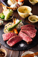 【黒毛和牛ステーキ】レアで美しく焼き上げた黒毛和牛モモ肉のステーキ。ジューシーな肉の旨みを引き立てるのは、素揚げした季節の野菜と彩り豊かな薬味。わさびや塩、日本酒とともに、和の美味を贅沢に味わう一皿です。
