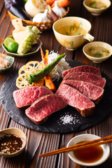 【黒毛和牛ステーキ】レアで美しく焼き上げた黒毛和牛モモ肉のステーキ。ジューシーな肉の旨みを引き立てるのは、素揚げした季節の野菜と彩り豊かな薬味。わさびや塩、日本酒とともに、和の美味を贅沢に味わう一皿です。