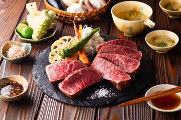 【黒毛和牛ステーキ】レアで美しく焼き上げた黒毛和牛モモ肉のステーキ。ジューシーな肉の旨みを引き立てるのは、素揚げした季節の野菜と彩り豊かな薬味。わさびや塩、日本酒とともに、和の美味を贅沢に味わう一皿です。
