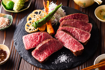 【黒毛和牛ステーキ】レアで美しく焼き上げた黒毛和牛モモ肉のステーキ。ジューシーな肉の旨みを引き立てるのは、素揚げした季節の野菜と彩り豊かな薬味。わさびや塩、日本酒とともに、和の美味を贅沢に味わう一皿です。