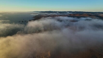 Aerial view of a dramatic coastline where fog rolls inland, obscuring the hills and meeting the sea, creating a serene yet powerful scene, California, United States. - Powered by Adobe