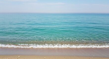 Turquoise ocean waves gently wash onto a sandy beach under a clear sky