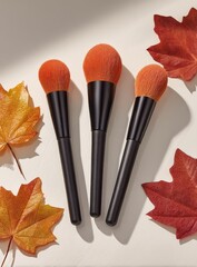 Three orange makeup brushes with black handles, displayed amongst autumn leaves