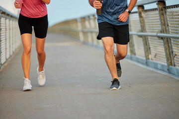 Two individuals are jogging together on a boardwalk in a pleasant outdoor setting during the early...