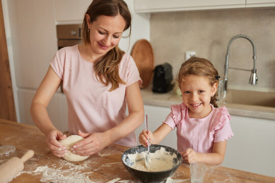 In a warm kitchen, a mother and daughter bond over baking as they knead dough and mix ingredients, sharing laughter and joy during their creative culinary time together. - Powered by Adobe