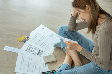 Stressed and headache asian woman with large bills or invoices no money to pay to expenses and...