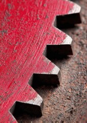 Close-up of a red-painted, serrated metal gear resting on a rusty surface, showing texture and wear