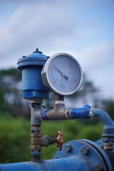 A close-up of a water pressure gauge mounted on a blue industrial pipe outdoors