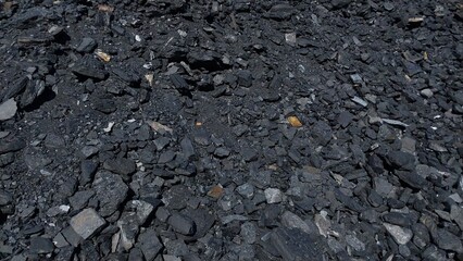 A close-up of dark, coarse gravel and small stones scattered across a rough ground surface, with...