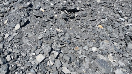 A close-up view of a rough, rocky surface covered in gray gravel and small stones, with scattered patches of green moss or grass growing between the cracks