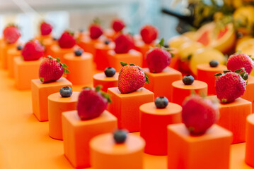 Ripe red strawberries lie on orange cubes next to raspberries