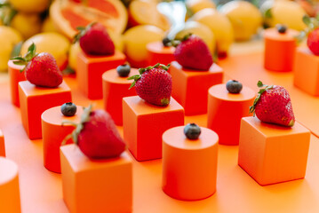 Ripe red strawberries lie on orange cubes next to raspberries