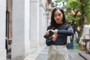 Asian businesswoman using her smartwatch and smartphone while walking in a modern city setting