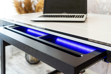 Top view of open wooden drawer white office table with blue lightning. Modern office table with...