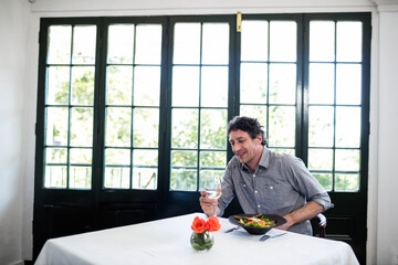 Wine glass is resting on white tablecloth in dining area, with orange roses by grid windows