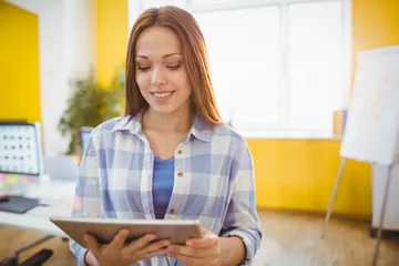Fotobehang Office worker holding tablet, reading screen at desk with monitor and potted plant in yellow office © WavebreakMediaMicro