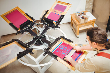 Screen printing press rotating on carousel in studio dispensing inks onto screens and supply cart